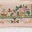 White rectangular postcard with embroidered scene depicting two brown sail boats and vase of pink flowers.  