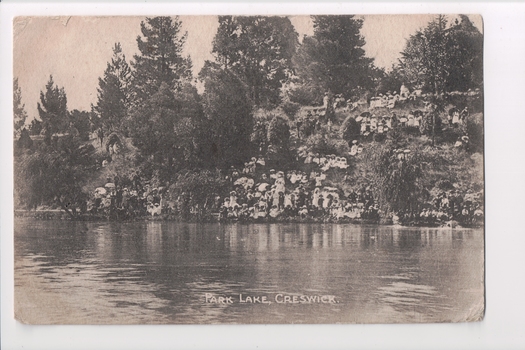Black and white postcard of steep bank with trees leading down to wide river