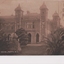 Postcard of sepia photograph of large building with turrets with large shrubs in foreground