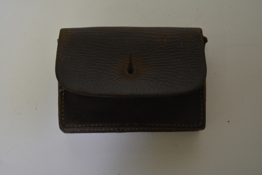 Brown leather pouch with front flap and two belt keepers on the back. Has large yellowing stitching.