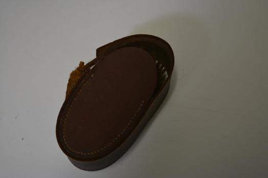 Brown leather pouch containing a wooden brush.  Flap is locked by a metal buckle.  Has large yellowing stitching.