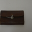 Brown leather pouch/wallet.  Has tan interior with pen in writing inside.  Has large silver metal catch on front.