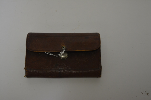 Brown leather pouch/wallet.  Has tan interior with pen in writing inside.  Has large silver metal catch on front.