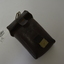 Small dark brown leather pouch with engraving on the back and on the front has lines engraved into the leather.  Has a canvas and metal buckle with a metal hanger on the top.