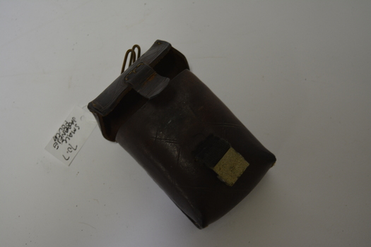 Small dark brown leather pouch with engraving on the back and on the front has lines engraved into the leather.  Has a canvas and metal buckle with a metal hanger on the top.