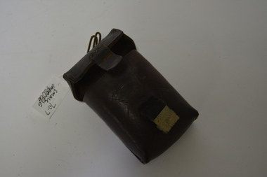 Small dark brown leather pouch with engraving on the back and on the front has lines engraved into the leather.  Has a canvas and metal buckle with a metal hanger on the top.