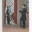 Colour postcard of two men, one wearing hat and holding umbrella at front  door of a house.