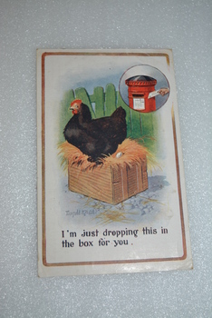 Postcard with a colour illustration of a black hen sitting on a crate of straw.  Green palings in background.  Round insert with a 'old style' red mail box.