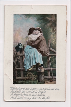 Man wearing straw boater hat and woman wearing green skirt sitting on a fence embracing one another