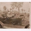 Photograph of three soldiers sitting in topless vehicle with hills and trees in background