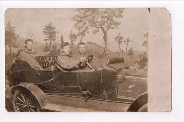 Photograph of three soldiers sitting in topless vehicle with hills and trees in background