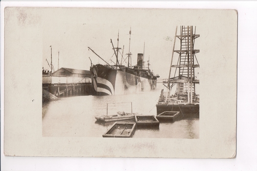 Ship docked alongside pier with barges in foreground