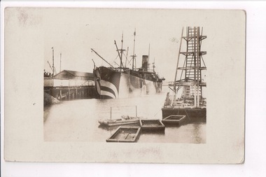 Ship docked alongside pier with barges in foreground