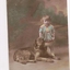 Small child standing next to dog lying down with background of green trees