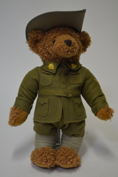Brown teddy bear, wearing WW1 Lance Corporal Army uniform with rising sun badges on collar, slouch hat and 59th Battalion patch on right shoulder.