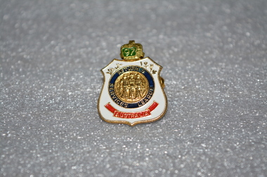 Gold badge with white on outside, crown on top, blue circle in the middle with gold in centre, Has red banner at bottom.