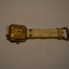 Gold coloured metal watch with square face and white plastic watch band.