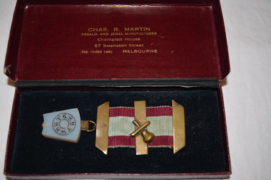 Maroon coloured presentation box containing maroon with blue stripe ribbon with three metal bars attached above white stone medal.
