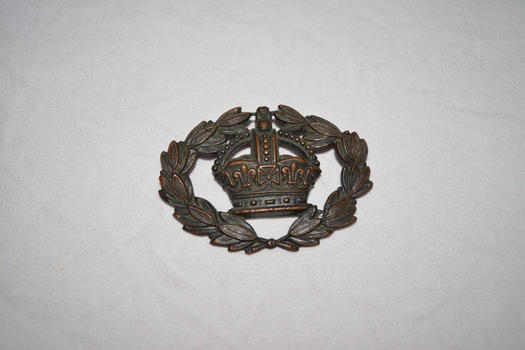 Brass coloured oval shape badge of crown encircled by laurel leaves