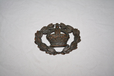 Brass coloured oval shape badge of crown encircled by laurel leaves