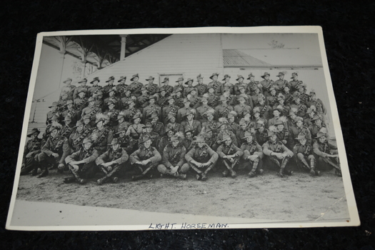 Black and white unframed photograph of large troop of Light Horse soldiers taken at side of a grandstand.