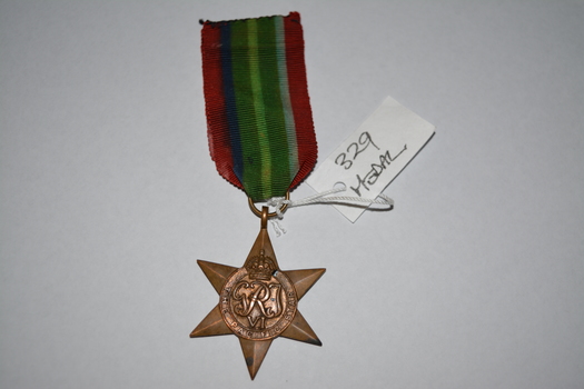Brass coloured star shaped medal with red blue green and black ribbon