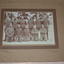 Sepia photograph of 11 men six standing and five kneeling dressed in military uniform wearing forage cap with row of pine trees in background.  Photograph is mounted on brown cardboard with handwriting across top border.