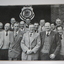 Black and white unframed group photograph of 14 men standing under RSL Logo shield.