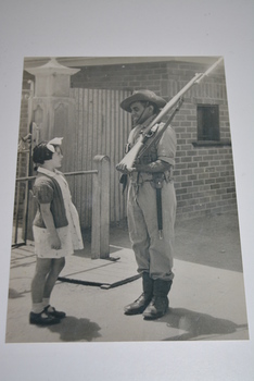 Black and white photograph of soldier with shouldered rifle talking to little girl