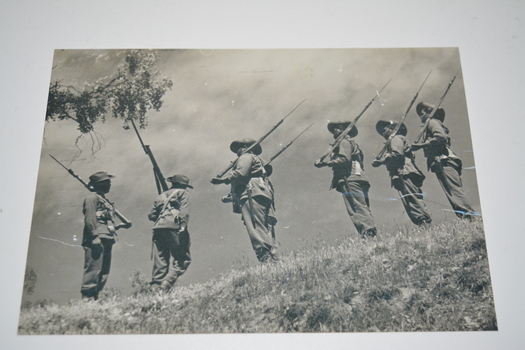  Black and white photograph of seven soldiers with shouldered rifles in single file
