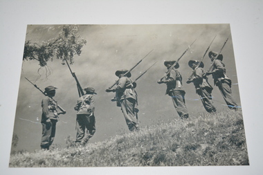  Black and white photograph of seven soldiers with shouldered rifles in single file
