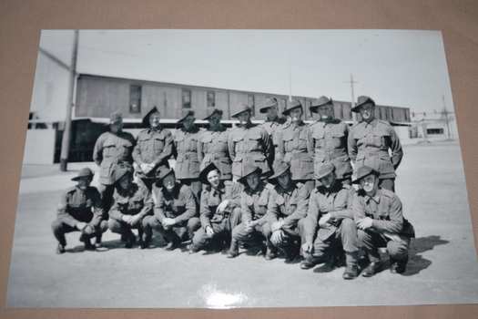 Two rows of soldiers wearing slouch hats, half standing others kneeling in front of large  building in background
