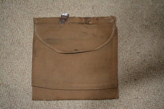 Brown canvas double sided pouch bag that has a brown cloth overlay. Attached on top is small metal ring near  tear repaired by hand stitching.