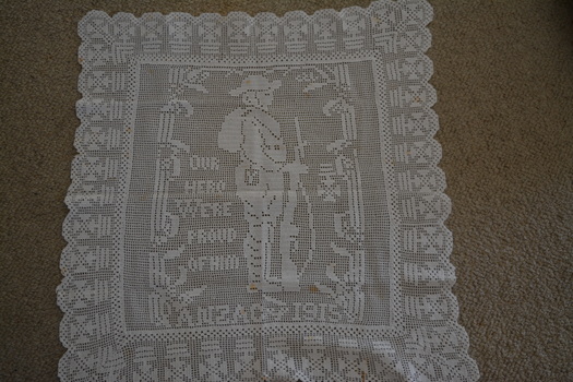 Off white square crocheted doily with side on image of soldier holding rifle in the centre.