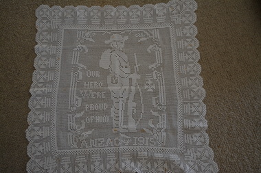 Off white square crocheted doily with side on image of soldier holding rifle in the centre.