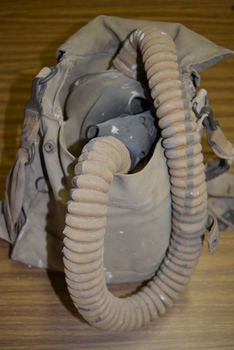 Canvas bag containing Small Box Respirator consisting of a rubberised fabric face mask, connected by a fabric covered rubber hose to a canister made of tin plate.