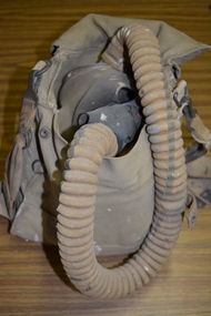 Canvas bag containing Small Box Respirator consisting of a rubberised fabric face mask, connected by a fabric covered rubber hose to a canister made of tin plate.