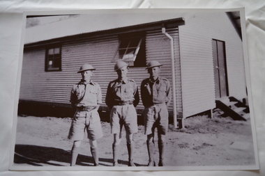 Three soldiers wearing tin hats standing in front of corrugated clad building
