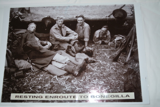 Group of four soldiers resting against large felled tree trunk.
