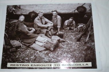 Group of four soldiers resting against large felled tree trunk.