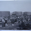 Large group of soldiers with packs/kit standing in front of row of trucks with canvas covers