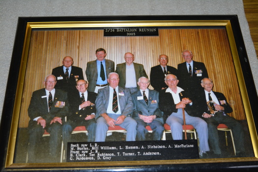 Group of eleven men wearing suits, five standing with 6 seated in front with list of names beneath