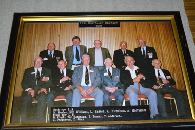 Group of eleven men wearing suits, five standing with 6 seated in front with list of names beneath