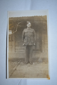 Black and white photograph  of soldier standing in front of weatherboard house