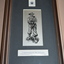 Silver plate frame with black mount containing sketch of soldier holding automatic rifle