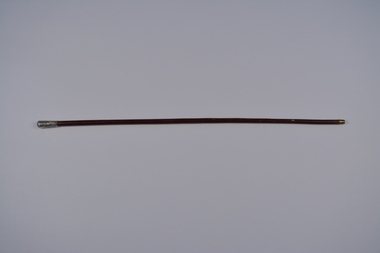 Long narrow round cane made from polished reddish/brown wood with brass metal tip and embossed silver top