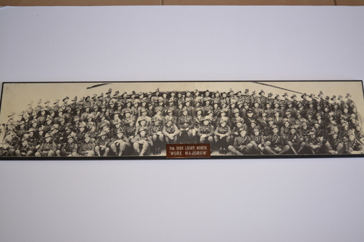 Wide and narrow rectangle shaped black and white reproduction photograph mounted on plyboard.  A small metal plaque is attached in the centre of lower edge.