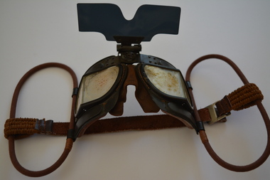 Black metal goggles with black plastic sun visor attached to circular brown cloth strapping