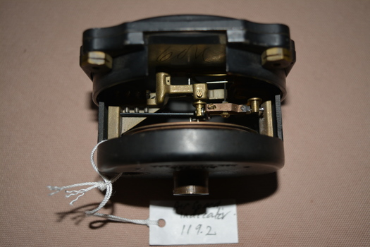 Black painted cylindrical instrument with glass face .  There is a side cutout containing  metal parts .