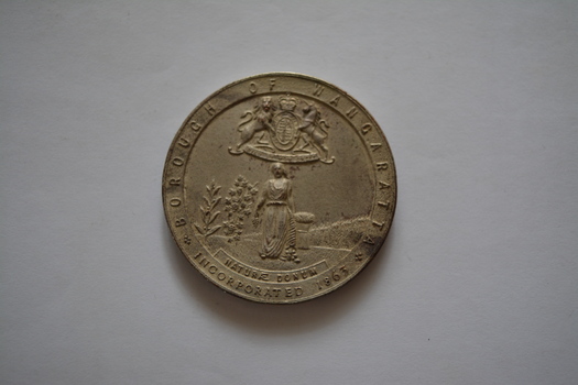 Circular silver metal medal- obverse side has coat of arms above image of woman in a field - rear side embossed with laurel wreath.